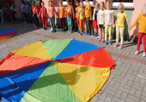 dzieci ustawione w kole tańczą na tarasie przedszkolnym wokół kolorowych chust